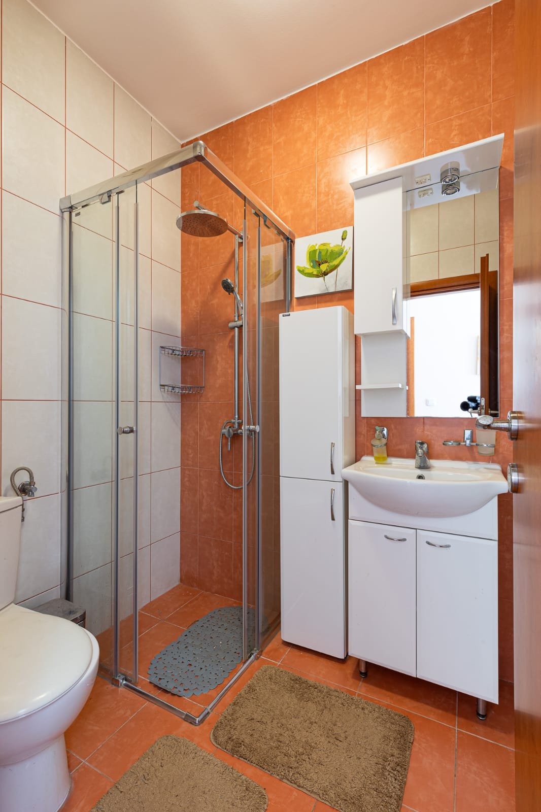 Modern Ulcinj bathroom with stylish orange-white tiles, glass shower, premium fixtures. Exclusive on immorenta.me by ekosphere doo.