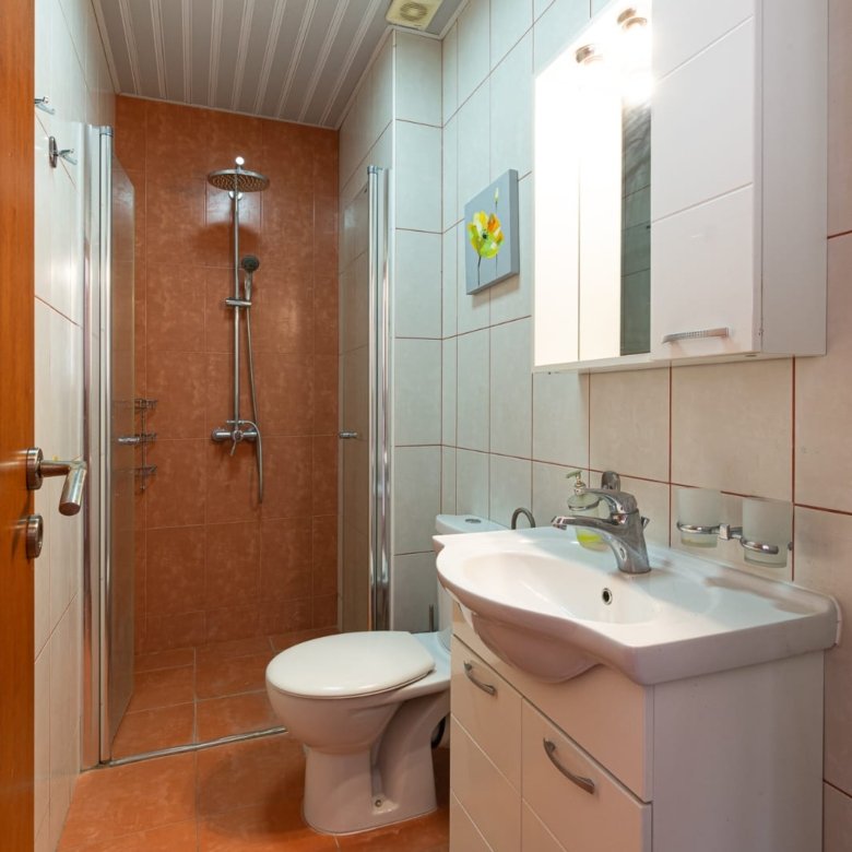 Modern, space-efficient bathroom in Ulcinj with orange tiles, premium fixtures, glass shower. Invest via immorenta.me by ekosphere doo.