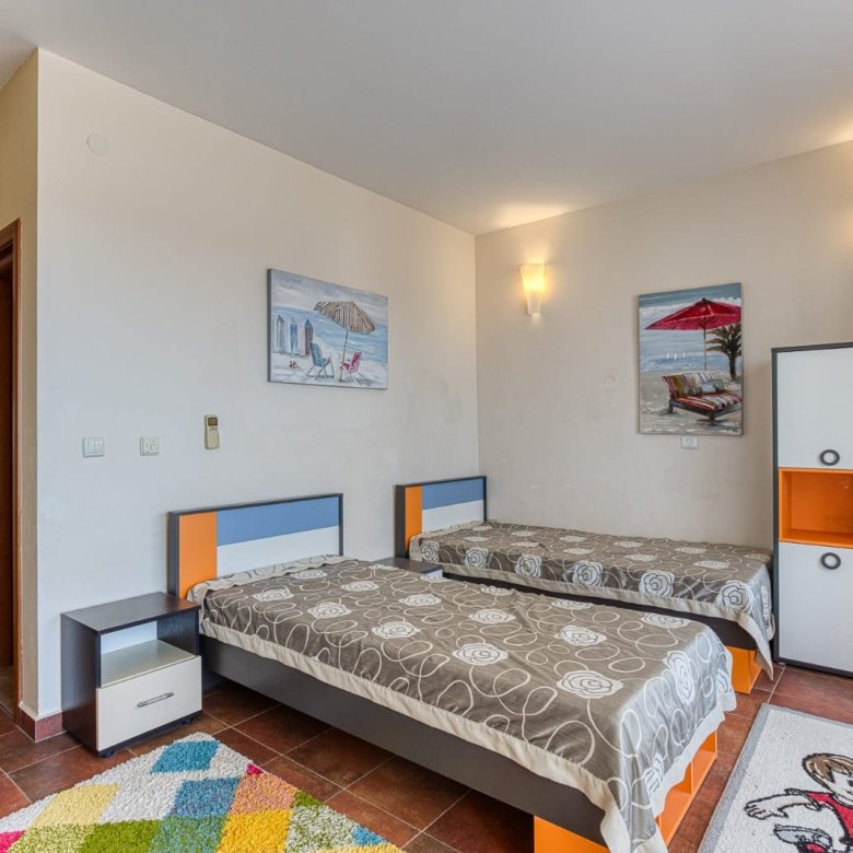 Bright Ulcinj bedroom with twin beds, wardrobe, modern lights, colorful rug, and sunny window&mdash;exclusive at Montenegro-Listings.me by Ekosphere Doo.