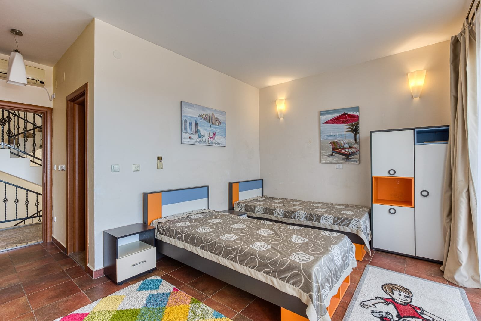 Bright Ulcinj bedroom with twin beds, wardrobe, modern lights, colorful rug, and sunny window&mdash;exclusive at Montenegro-Listings.me by Ekosphere Doo.