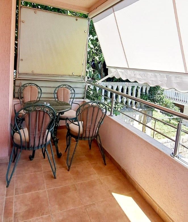 Stylish tiled balcony in Ulcinj with glass table, 4 cushioned chairs, greenery views. Invest via immorenta.me by ekosphere doo.