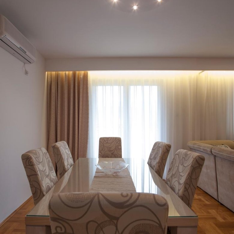 Elegant Ulcinj dining area: glass table, designer chairs, sunlit windows, chic lighting, hardwood floors. Invest via immorenta.me by ekosphere doo.