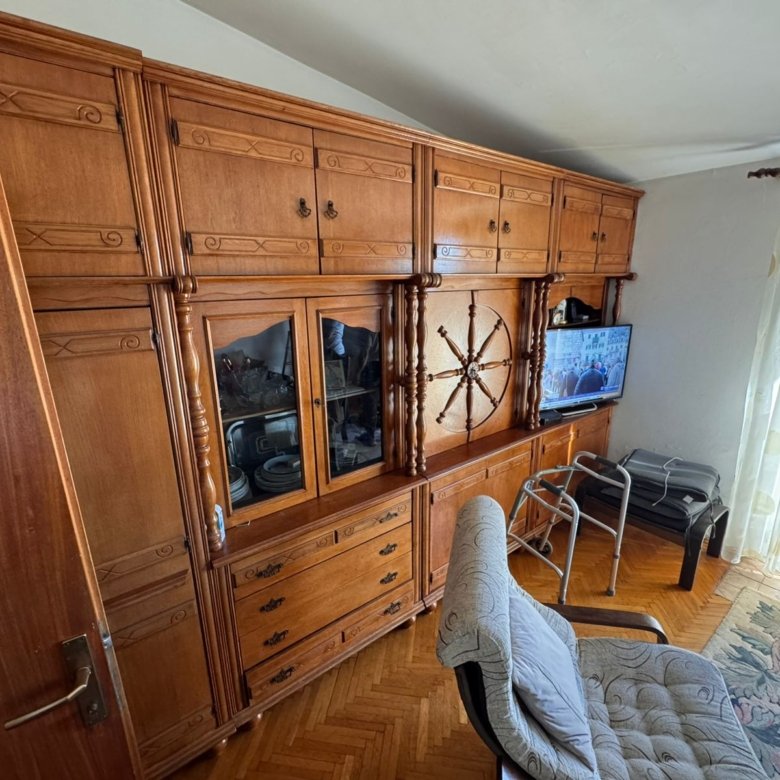 Elegant wooden wall unit with glass cabinets, TV, and cozy seating by a bright window&mdash;ideal Ulcinj real estate investment.