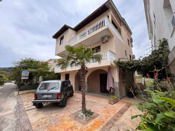Elegant three-story beige villa with balconies, lush greenery, palm tree, and private driveway in Ulcinj. Listed on immorenta.me by ekosphere doo&mdash;prime real estate investment opportunity!.