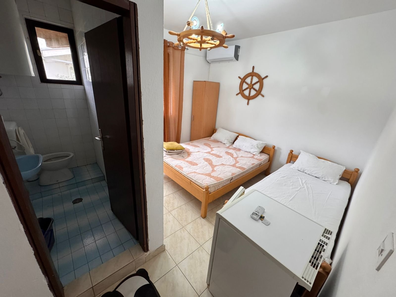 Charming Ulcinj hotel room: double & single beds, mini fridge, unique decor, ensuite with blue tiles. Invest via immorenta.me.