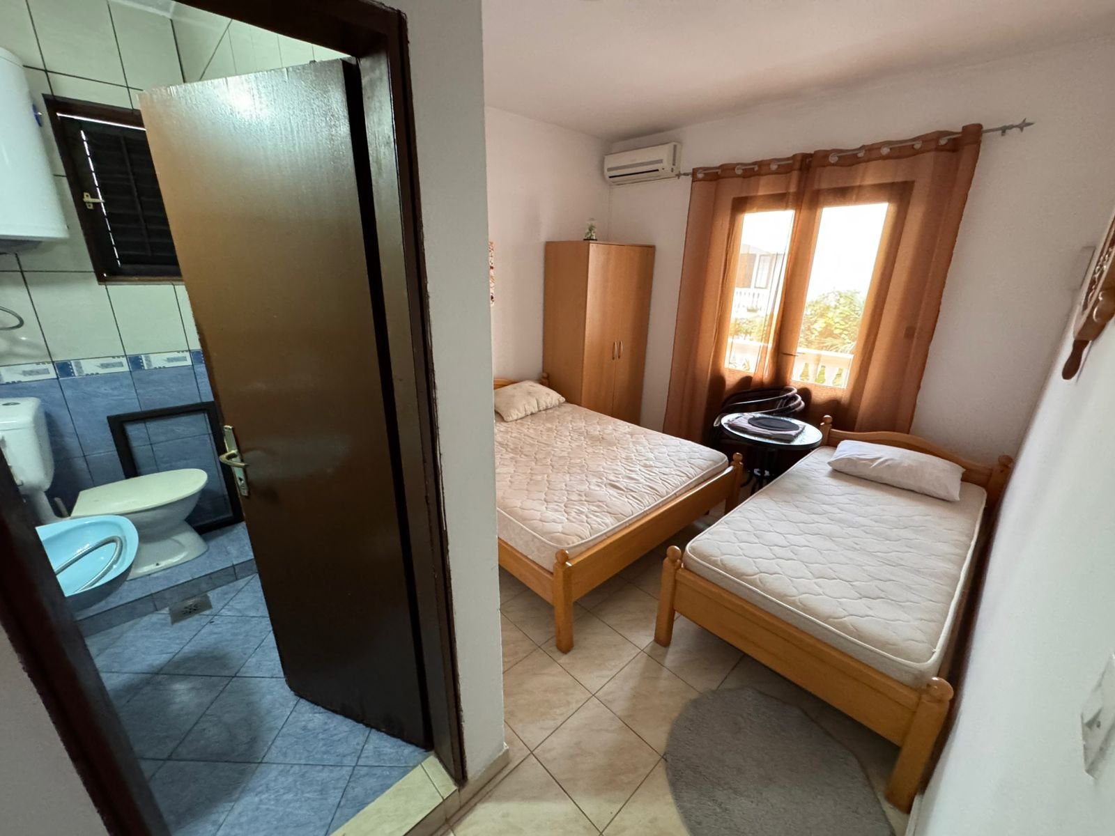 Bright Ulcinj bedroom with twin beds, wardrobe, window, and modern tiled bathroom&mdash;an ideal investment via immorenta.me.