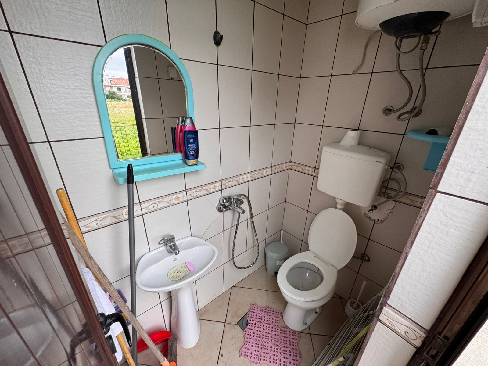 Modern tiled bathroom featuring a sink, mirror, and toilet, water heater, pink mat; ideal Ulcinj investment via immorenta.me.