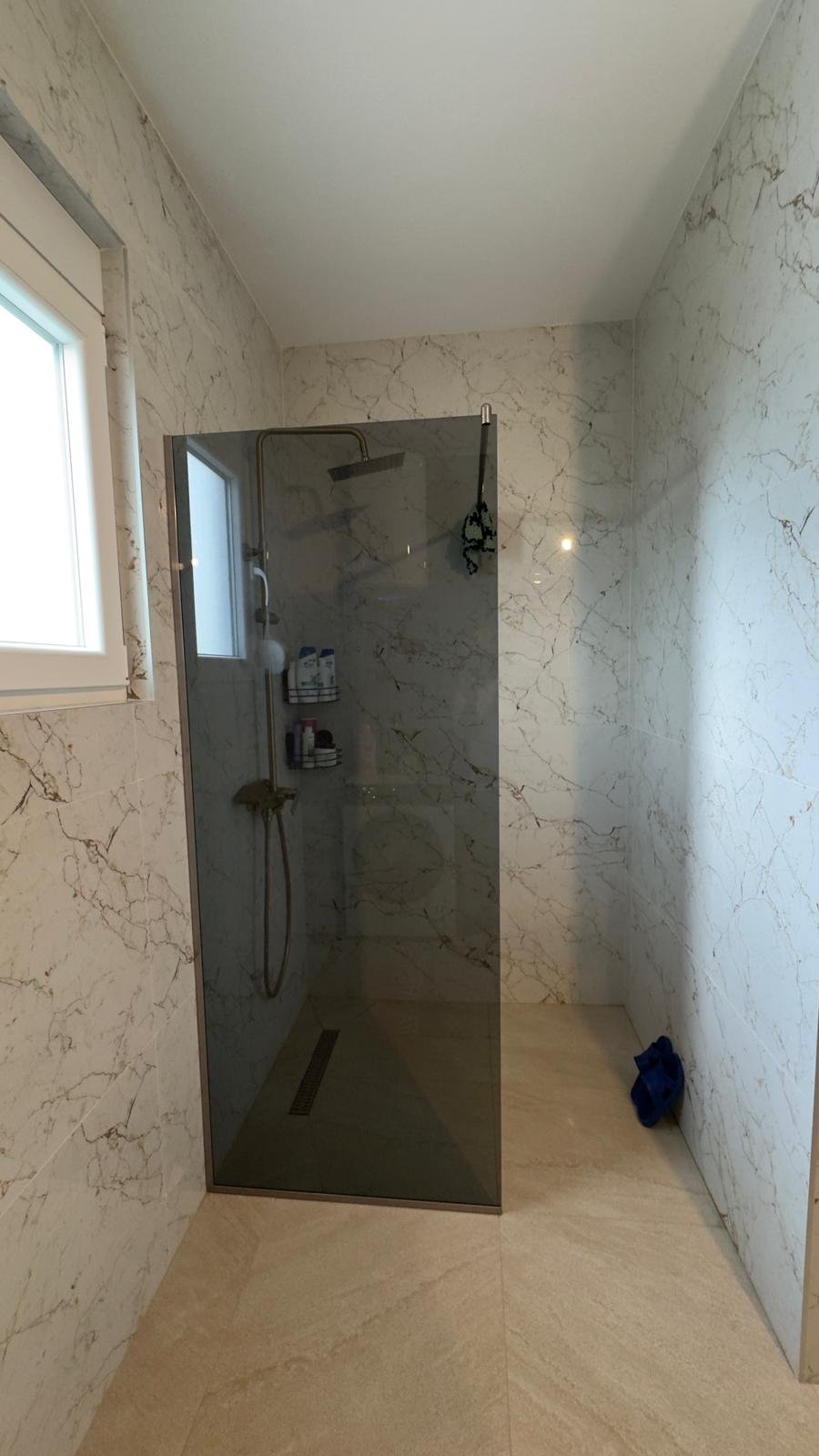 Elegant Ulcinj bathroom with beige marble, walk-in glass shower, window; premium investment on immorenta.me by ekosphere doo.