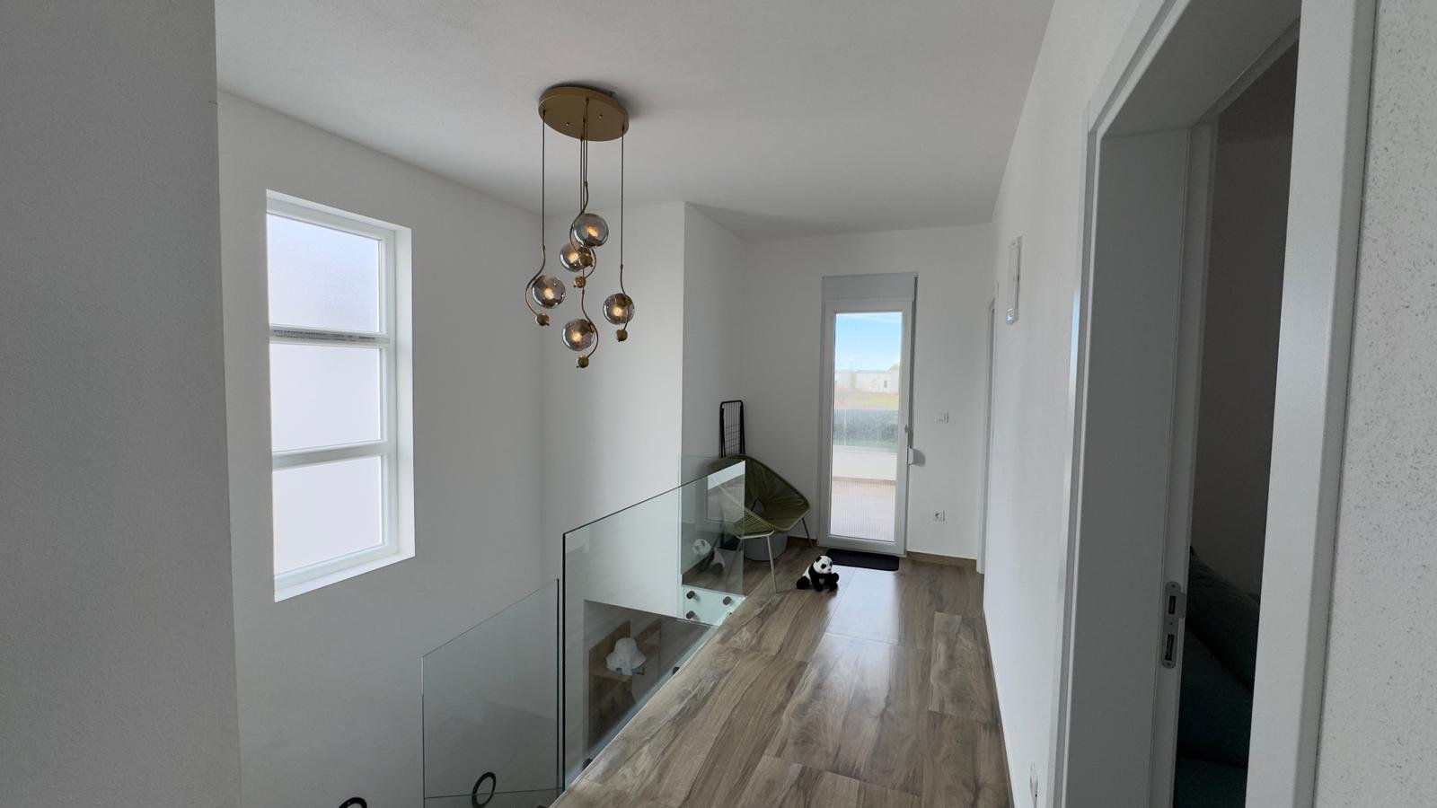 Elegant hallway in Ulcinj home with wood floors, modern chandelier, glass railing&mdash;exclusive property via immorenta.me by ekosphere doo.