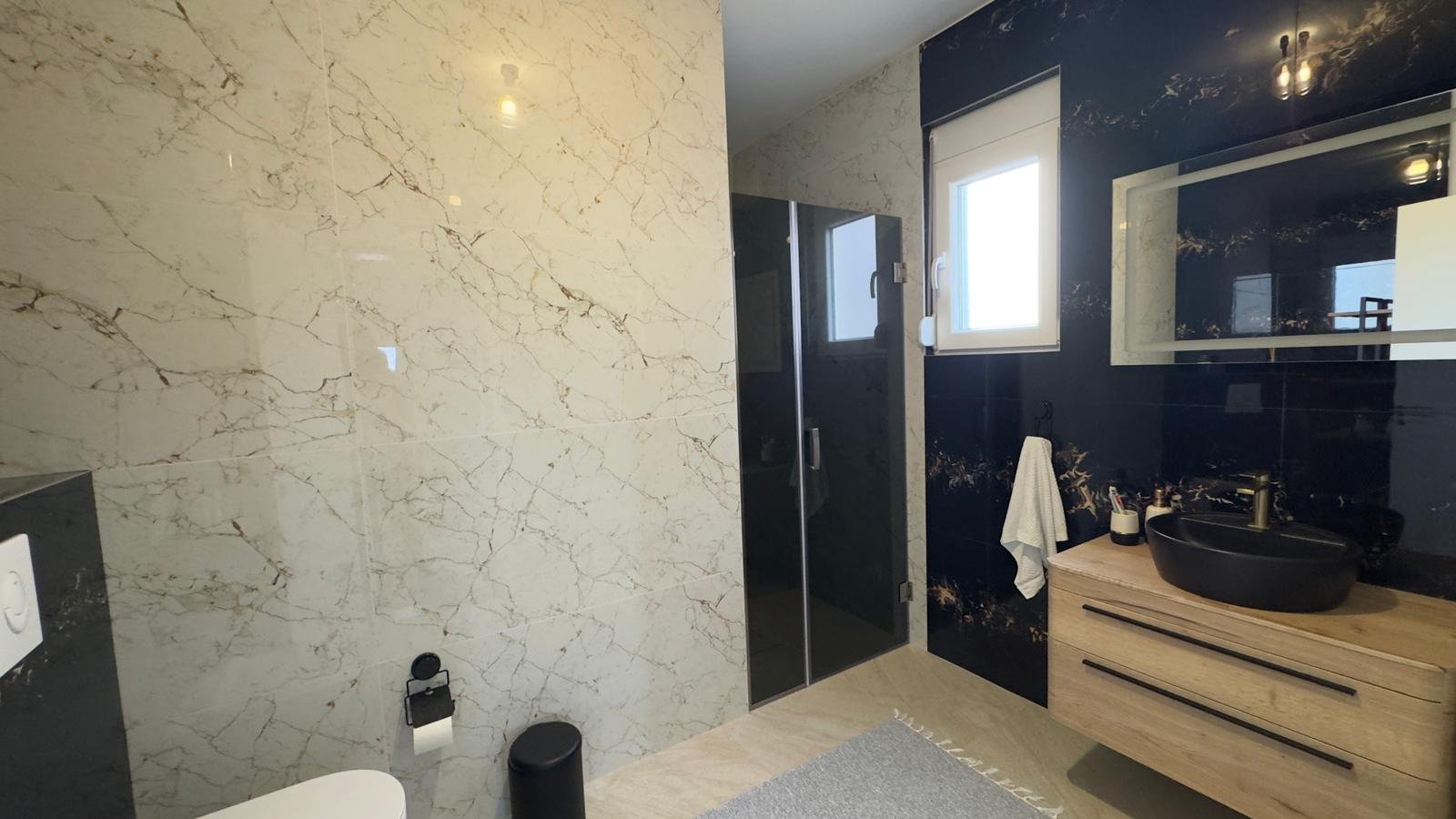 Elegant Ulcinj bathroom: marble-patterned walls, glass shower, luxury vanity&mdash;ideal Montenegro investment. By ekosphere doo.