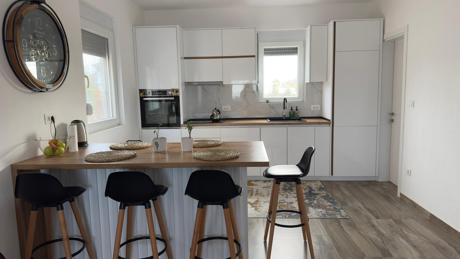 Sleek white kitchen in Ulcinj with wood counters, bar stools, built-in oven&mdash;ideal Montenegro property on immorenta.me by ekosphere doo.