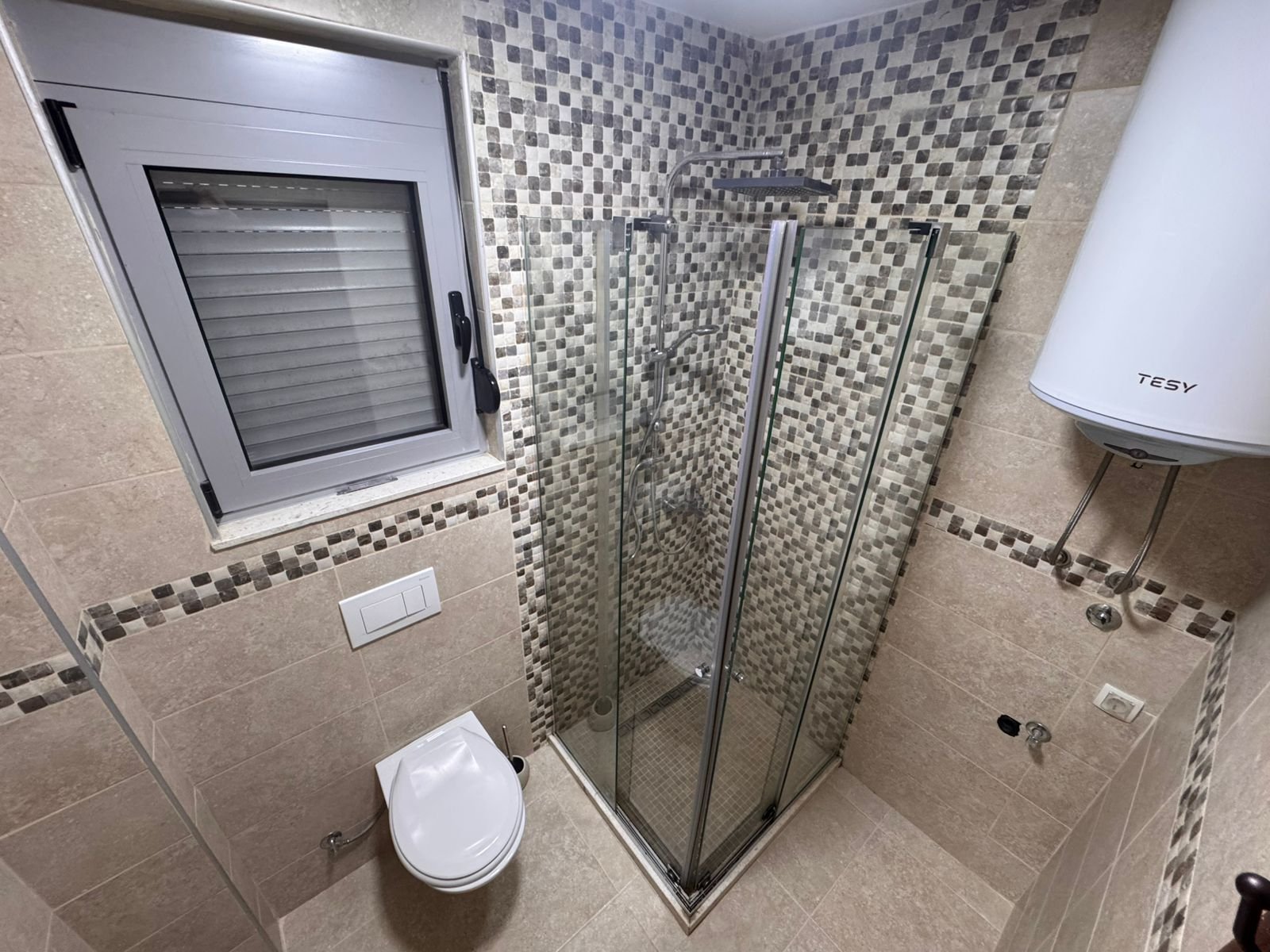Modern Ulcinj bathroom: beige tiles, glass corner shower, wall toilet, frosted window&mdash;investment property at immorenta.me by ekosphere doo.