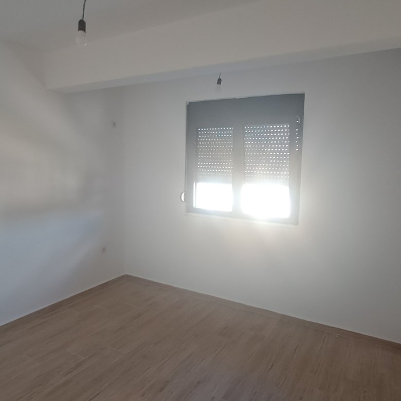 Bright, modern Ulcinj apartment with white walls, wood flooring, AC unit; sunlight through window. Invest via immorenta.me by ekosphere doo.