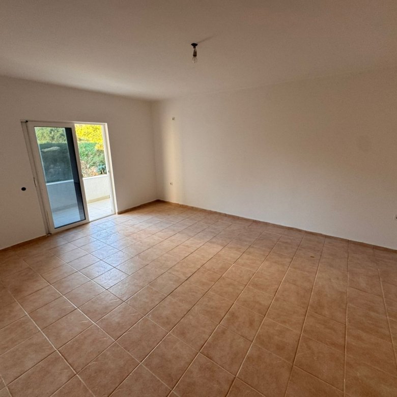 Bright, modern room in Ulcinj with beige tiled floors, white walls, and a balcony overlooking greenery&mdash;a prime Montenegro investment by ekosphere doo.