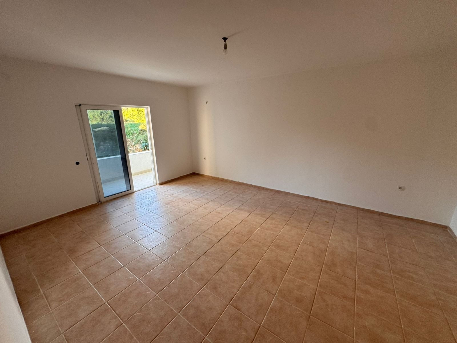 Bright, modern room in Ulcinj with beige tiled floors, white walls, and a balcony overlooking greenery&mdash;a prime Montenegro investment by ekosphere doo.