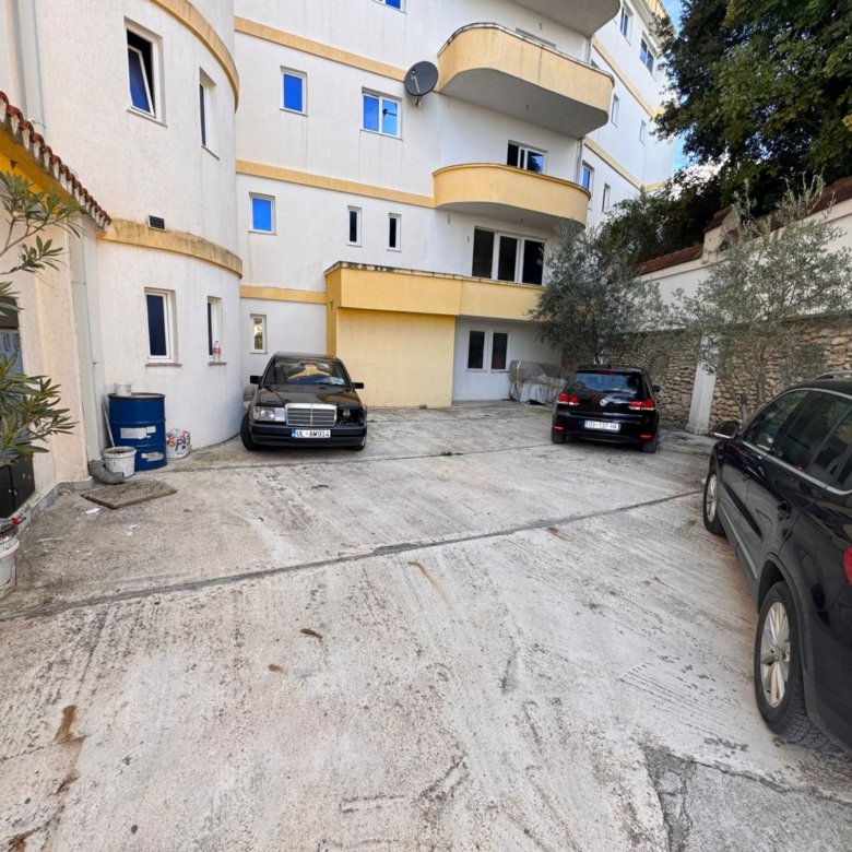 Prime Ulcinj investment: Multi-story cream-yellow building with parking, landscaped plants, stone wall. Listed on immorenta.me.