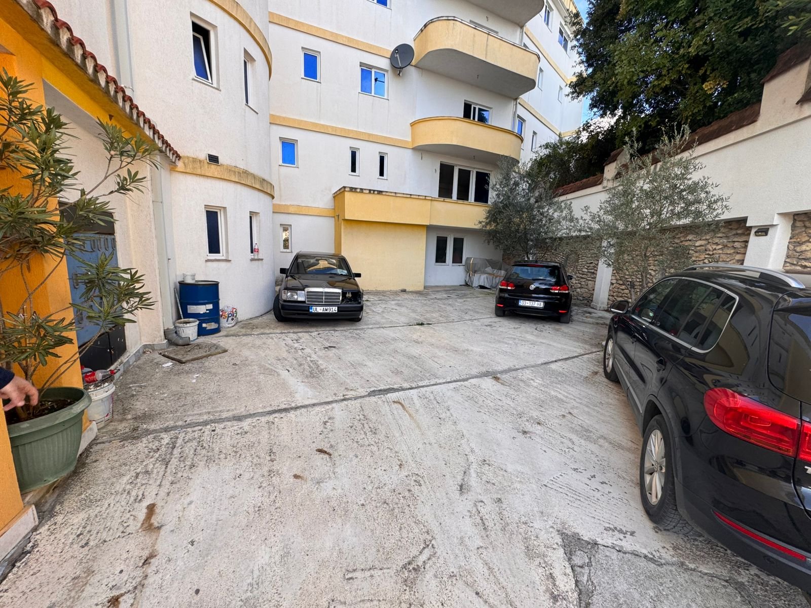 Prime Ulcinj investment: Multi-story cream-yellow building with parking, landscaped plants, stone wall. Listed on immorenta.me.