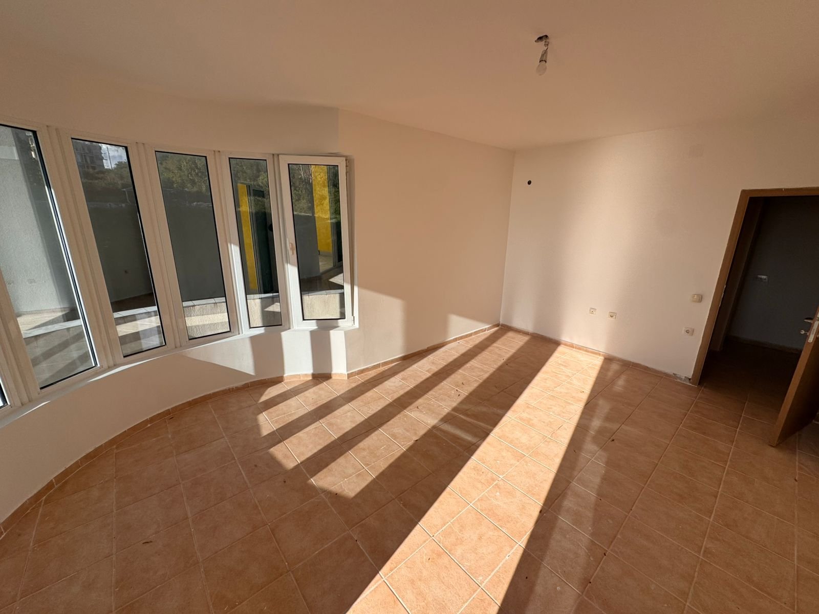 Bright, unfurnished Ulcinj property with tiled floors, curved panoramic windows, and cream walls. Featured on immorenta.me.