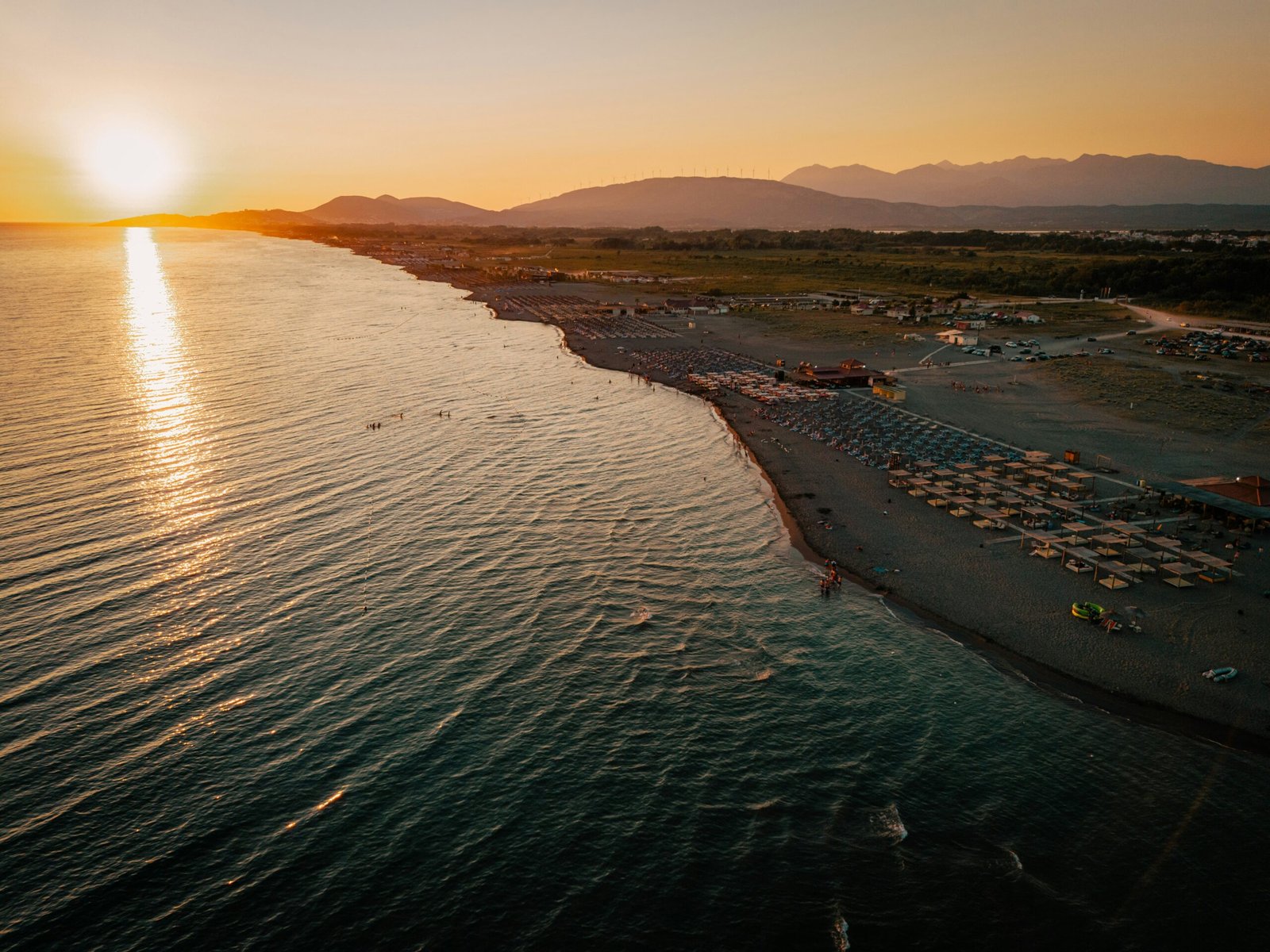 Entdecken Sie Ulcinj - Erstklassiger Strand von Ulcinj bei Sonnenuntergang mit Sonnenschirmen, Liegest&uuml;hlen, Meerblick und Bergen - exklusiv auf immorenta.me by ekosphere doo.