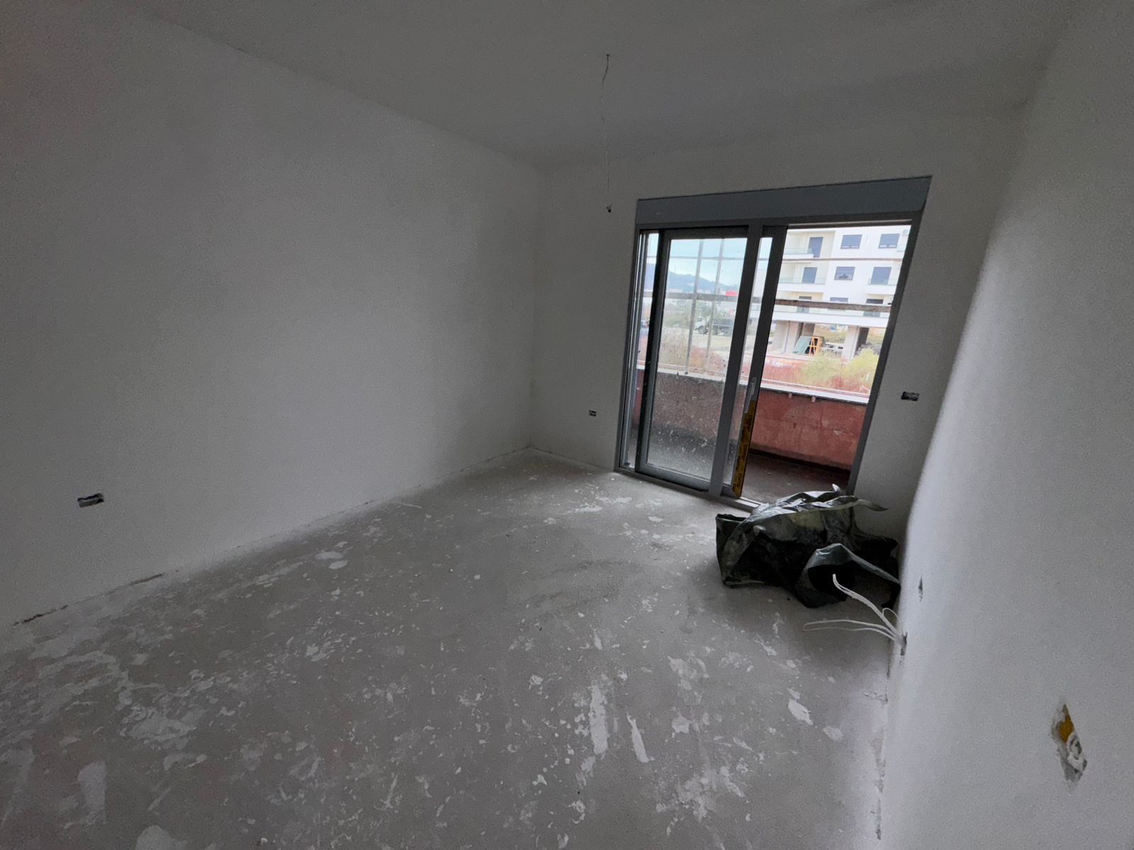 Spacious unfinished room in Ulcinj, Montenegro with white walls, concrete floors, and balcony access&mdash;prime investment via immorenta.me.