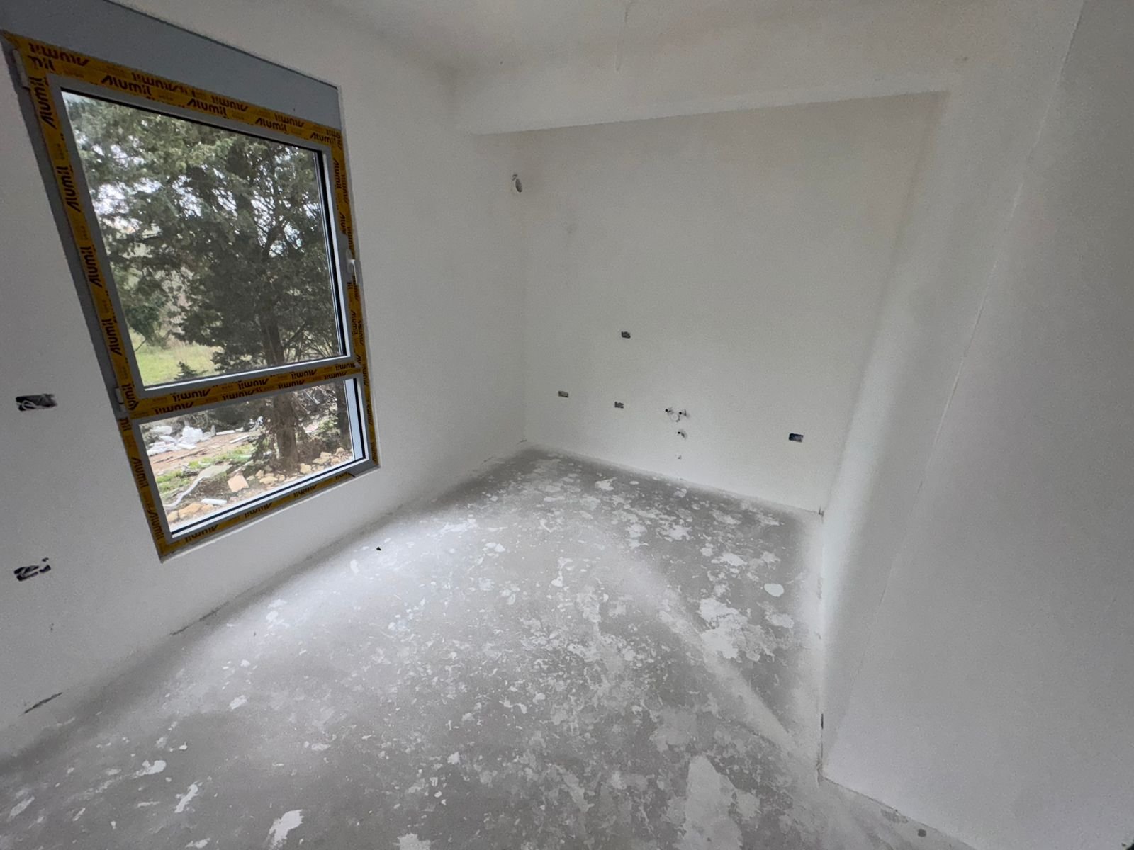 Unfinished room with white walls, concrete floor, large window&mdash;ideal for custom design in Ulcinj. Exclusive at immorenta.me by ekosphere doo.