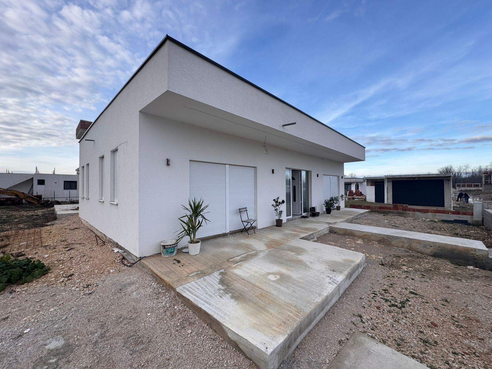 Contemporary 1-story white home in Ulcinj with flat roof, sliding glass doors, potted plants, and fenced yard&mdash;exclusive at immorenta.me.