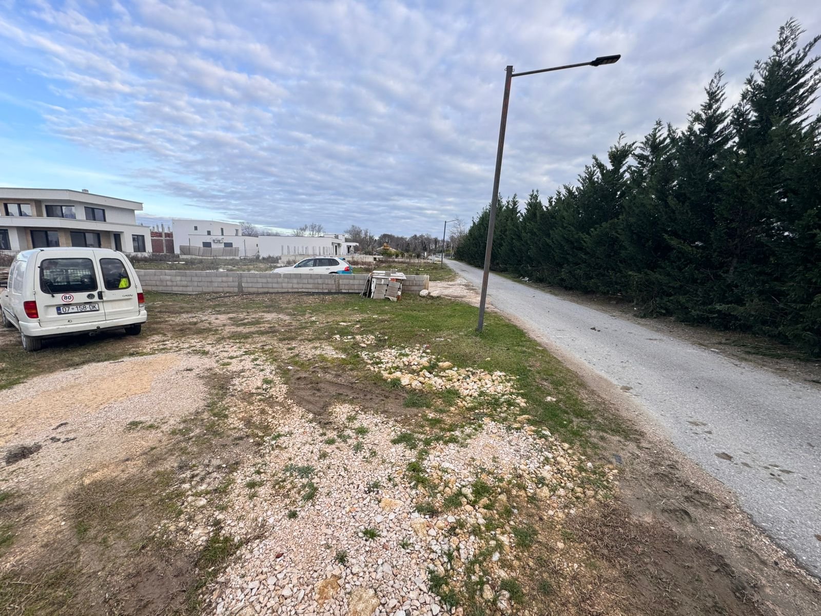 Prime Ulcinj land for sale: level dirt/gravel plot by paved road, evergreens, utilities nearby&mdash;ideal investment at immorenta.me.