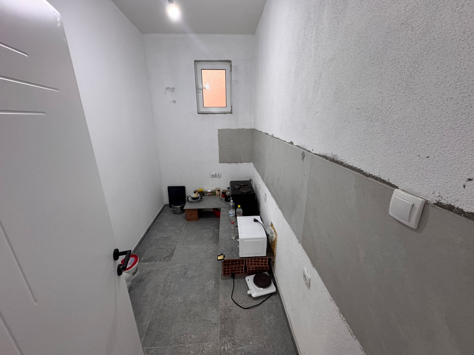 Investment opportunity in Ulcinj: unfinished compact space with gray tile floors, white walls, window. Exclusive on immorenta.me.