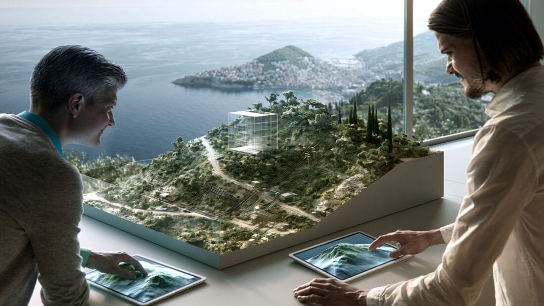 Vermögensstreuung - Zwei Personen prüfen auf Tablets ein Gebäudemodell in einer hügeligen Küstenlandschaft.