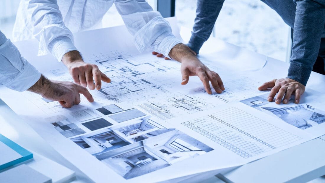 Due Diligence Drei Personen prüfen Baupläne, Objektfotos, Materialmuster und ein Diagramm auf einem Tisch.